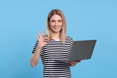 Photo of Happy woman with laptop showing ok gesture on light blue background