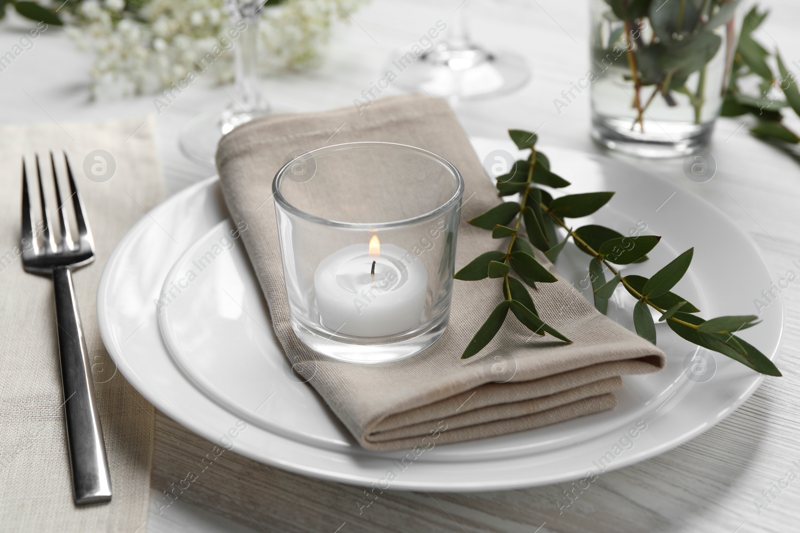 Photo of Stylish setting with cutlery, burning candle and eucalyptus leaves on white wooden table, closeup