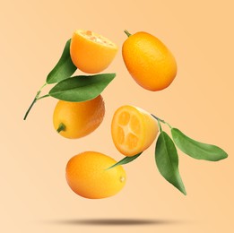 Image of Delicious fresh kumquats and green leaves falling on beige background