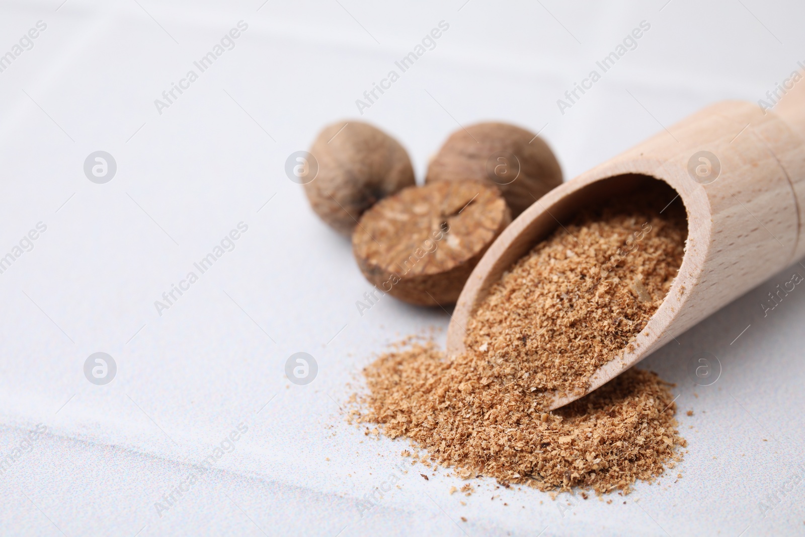 Photo of Scoop with grated nutmeg and seeds on white table, closeup. Space for text