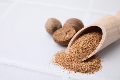 Scoop with grated nutmeg and seeds on white table, closeup. Space for text