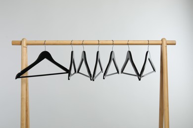 Photo of Black clothes hangers on wooden rack against light grey background