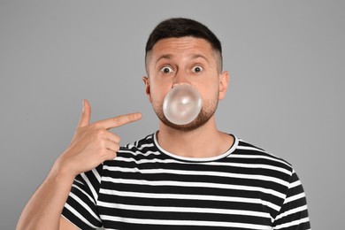 Surprised man blowing bubble gum on light grey background