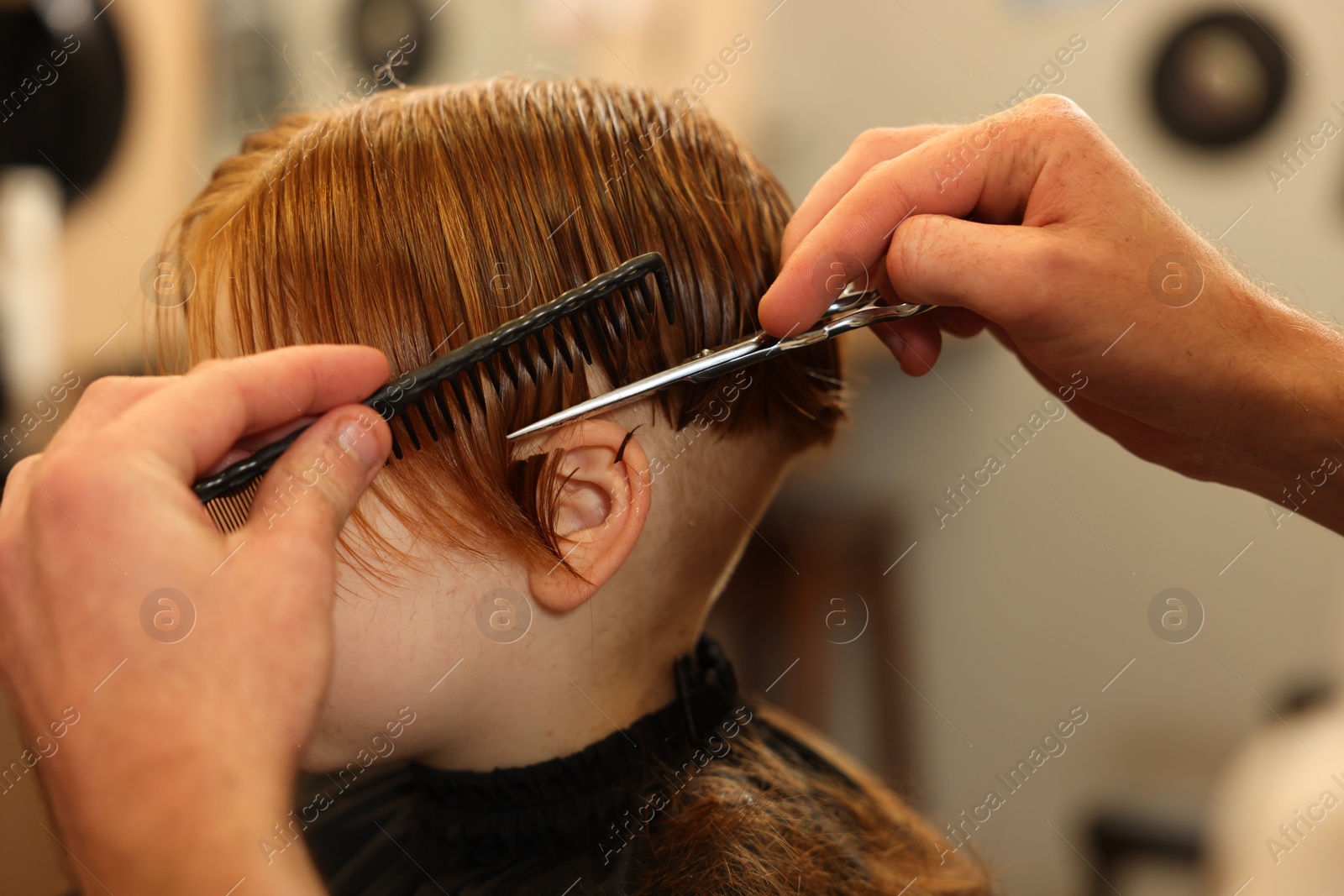 Photo of Professional hairdresser cutting boy's hair in beauty salon, closeup