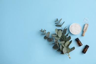 Photo of Aromatherapy products. Bottles of essential oil, sea salt and eucalyptus branches on light blue background, flat lay. Space for text