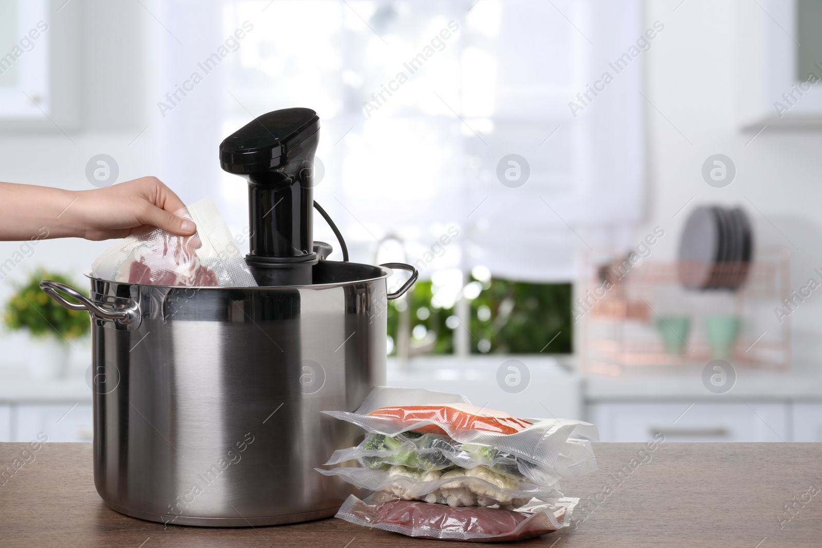 Image of Woman putting vacuum packed meat into pot with sous vide cooker on wooden table in kitchen, closeup. Thermal immersion circulator