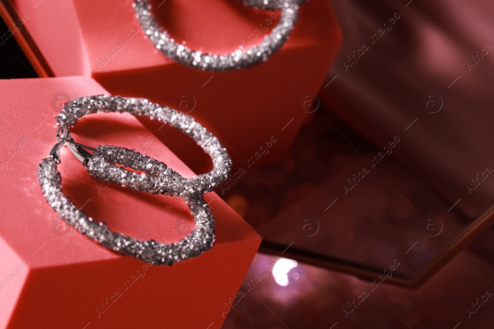 Photo of Elegant jewelry. Stylish presentation of luxury earrings on podium near mirror, closeup with space for text