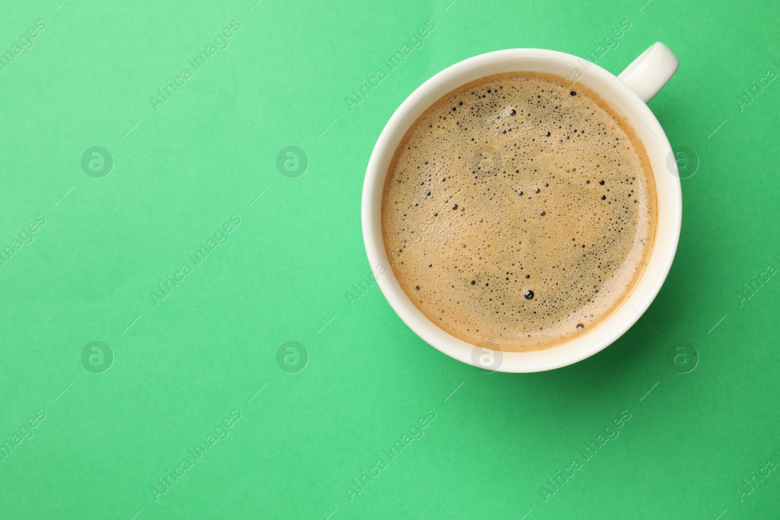 Photo of Aromatic coffee in cup on green background, top view. Space for text