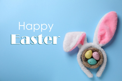 Image of Easter bunny ears headband and dyed eggs in nest on light blue background, flat lay