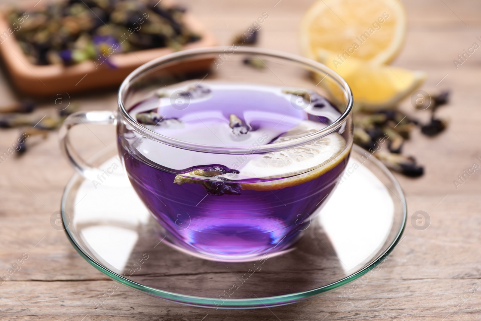 Photo of Glass cup of organic blue Anchan with lemon on wooden table, closeup. Herbal tea