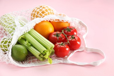 String bag with different vegetables and fruits on pink background, closeup