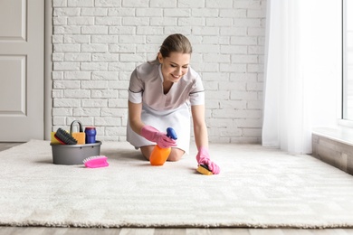 Photo of Chambermaid woman cleaning carpet indoors