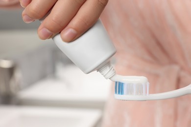 Woman applying toothpaste on brush in bathroom, closeup