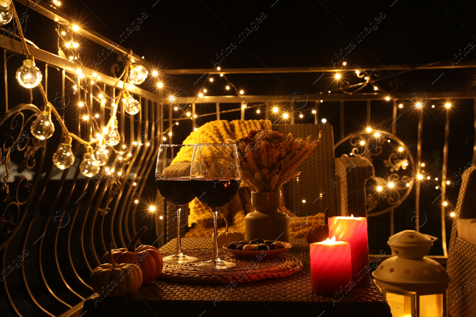 Photo of Glasses of wine, burning candles and decor on rattan table. Autumn evening on terrace