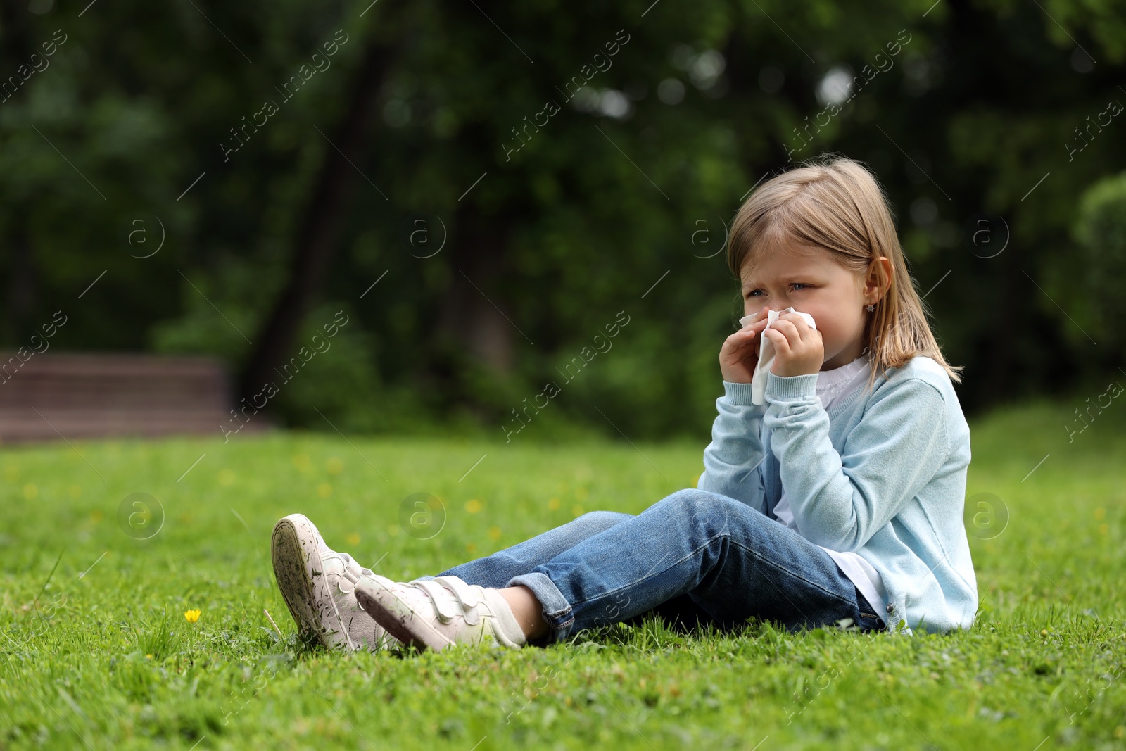 Photo of Little girl suffering from seasonal spring allergy on green grass in park