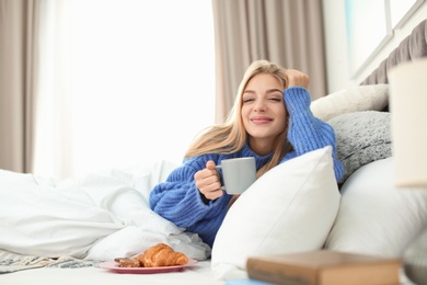 Photo of Beautiful young woman lying with breakfast in bed at home. Winter atmosphere