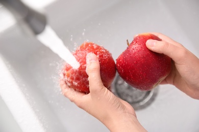 Woman washing fresh red apples in kitchen sink, top view