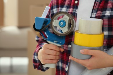Photo of Woman with handheld dispenser and rolls of adhesive tape indoors, closeup. Space for text