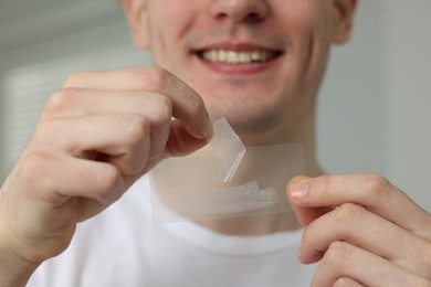 Photo of Young man with whitening strips indoors, closeup
