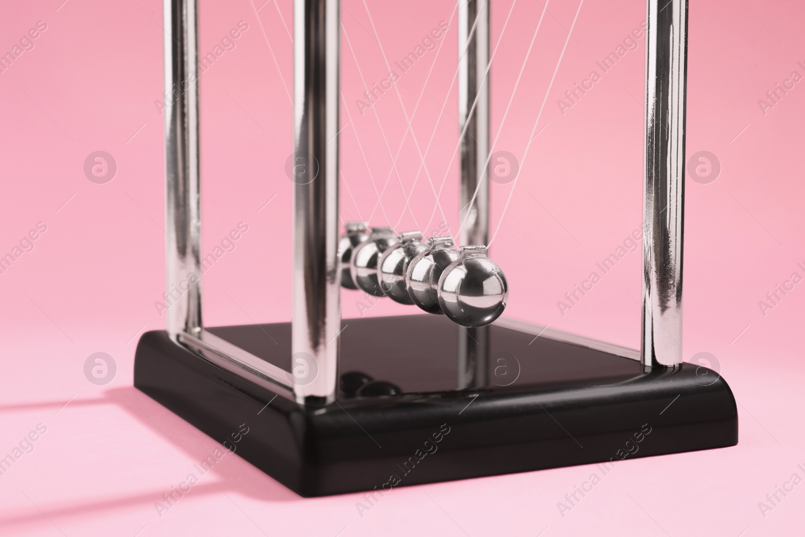 Photo of Newton's cradle on pink background, closeup. Physics law of energy conservation