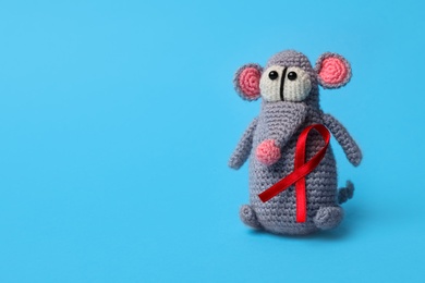 Photo of Cute knitted toy mouse with red ribbon on blue background, space for text. AIDS disease awareness