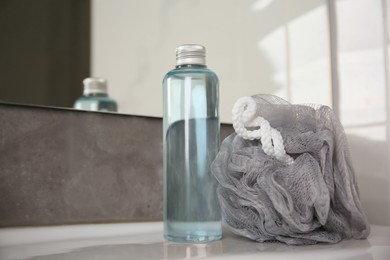 Photo of Grey sponge and shower gel bottle on washbasin in bathroom, closeup