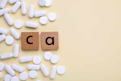 Photo of Wooden cubes with symbol Ca (Calcium) and pills on beige background, top view. Space for text