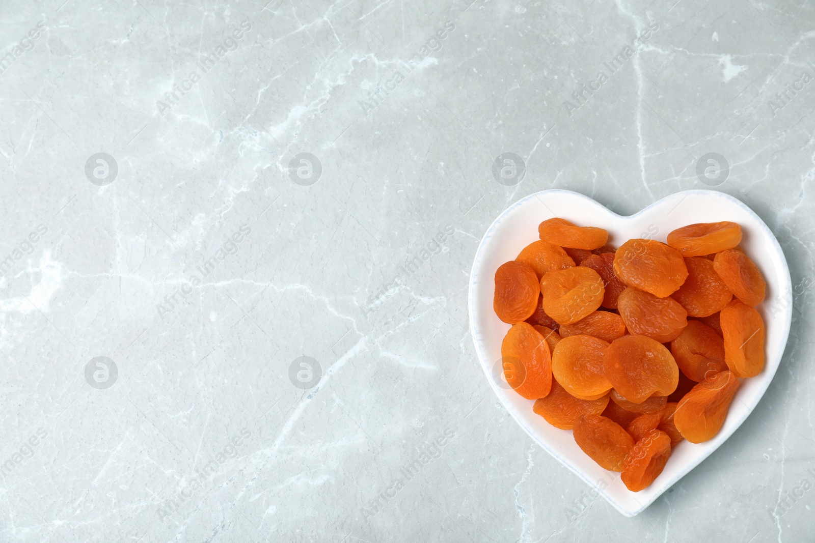 Photo of Plate of apricots on grey background, top view with space for text. Dried fruit as healthy food