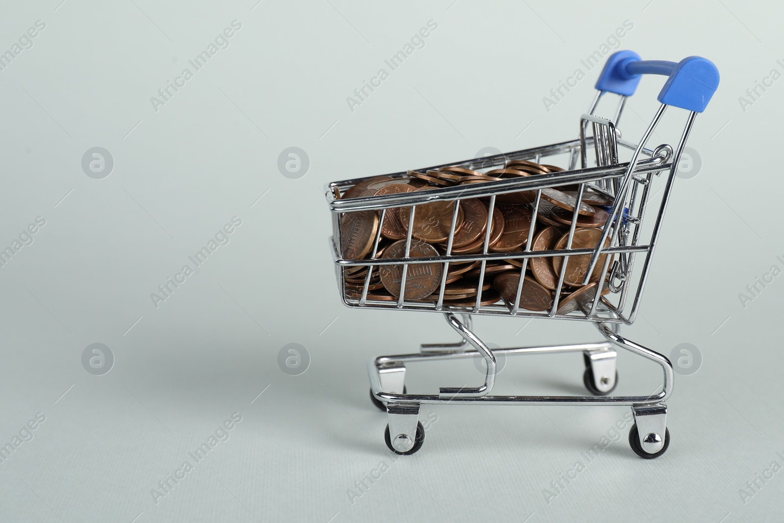 Photo of Small metal shopping cart with coins on light background, space for text