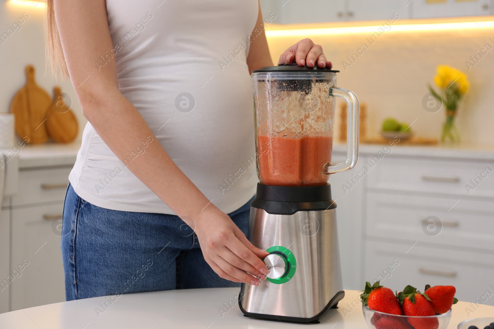 Photo of Young pregnant woman preparing smoothie at table in kitchen, closeup. Healthy eating