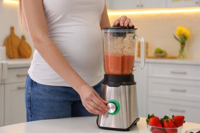 Photo of Young pregnant woman preparing smoothie at table in kitchen, closeup. Healthy eating