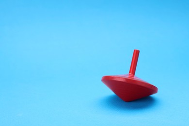 Photo of One bright spinning top on light blue background, space for text. Toy whirligig