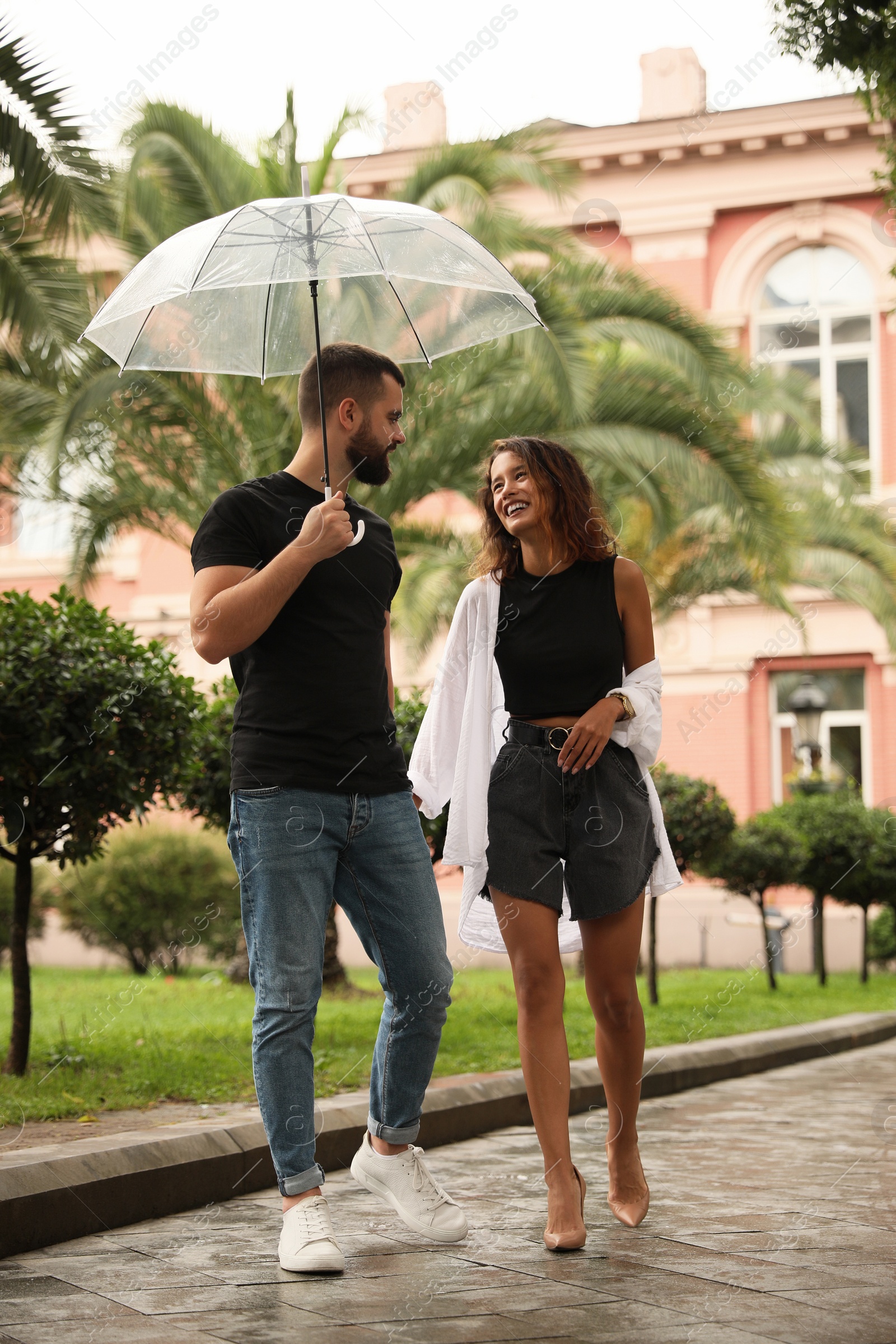 Photo of Young couple with umbrella enjoying time together under rain on city street