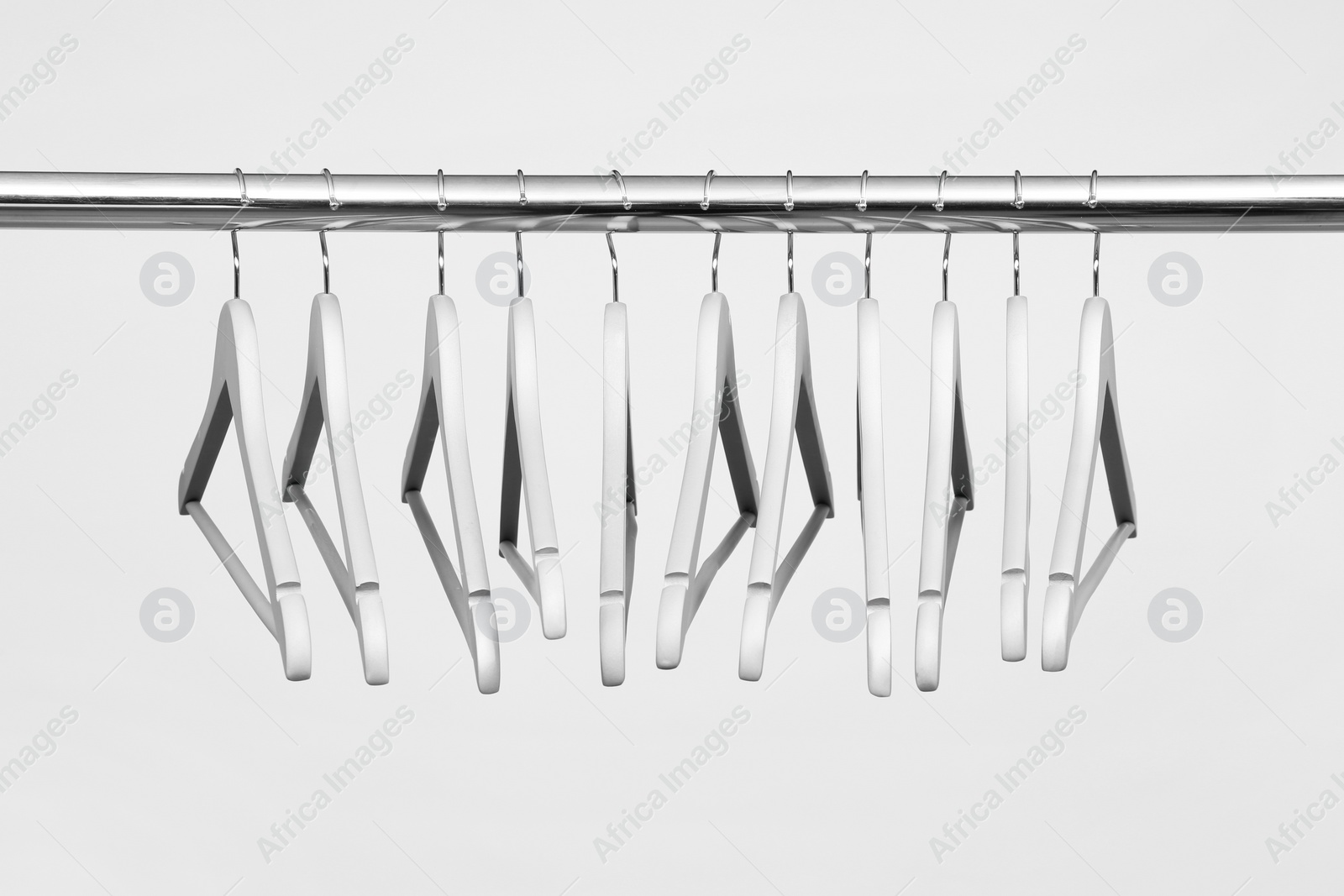 Photo of Empty clothes hangers on metal rail against light background