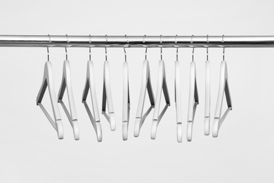 Photo of Empty clothes hangers on metal rail against light background