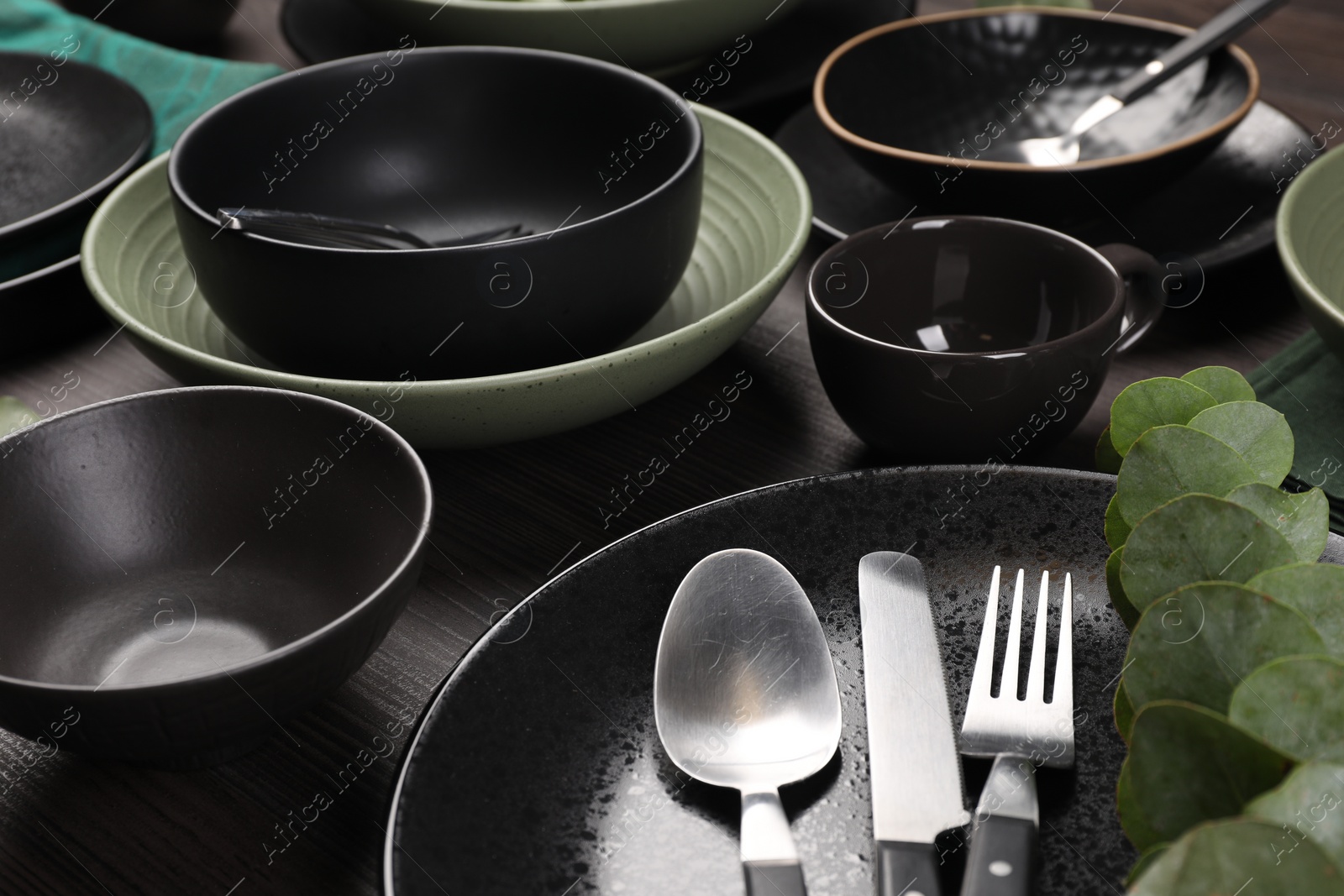 Photo of Stylish table setting with cutlery and eucalyptus branch on dark wooden background, closeup