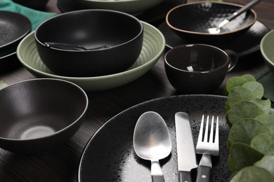 Stylish table setting with cutlery and eucalyptus branch on dark wooden background, closeup