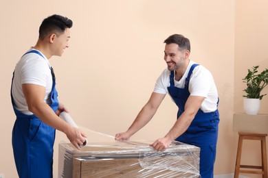 Workers wrapping chest of drawers in stretch film indoors