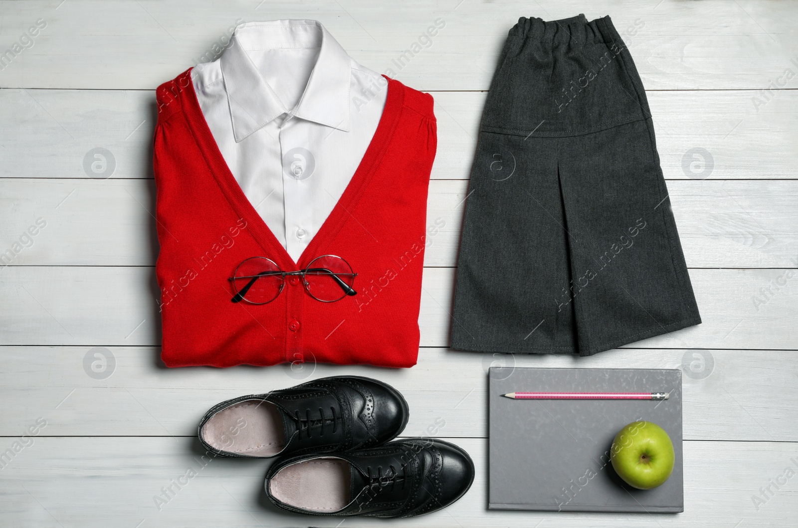 Photo of Stylish school uniform for girl, stationery and apple on white wooden background, flat lay