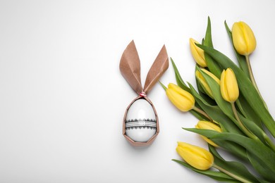 Easter bunny made of craft paper and egg near beautiful tulips on white background, flat lay. Space for text