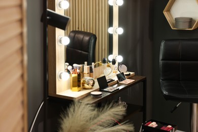 Makeup room. Stylish mirror with light bulbs and beauty products on dressing table indoors