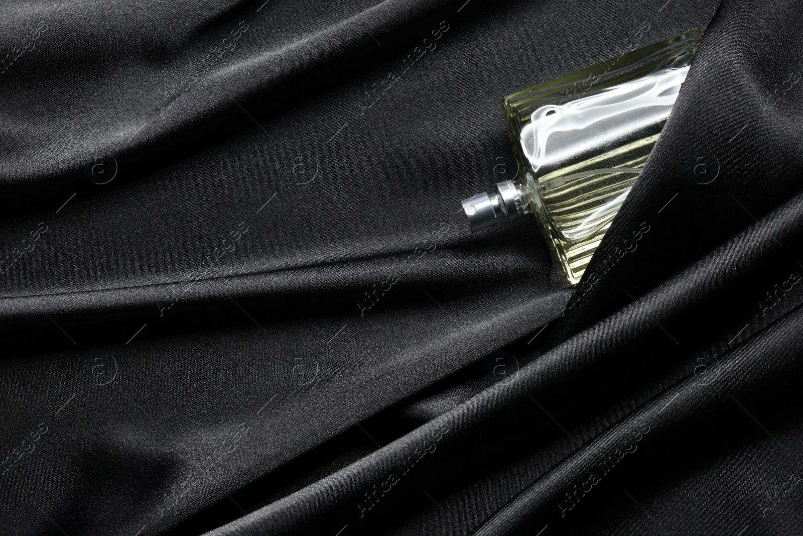 Photo of Luxury men's perfume in bottle on black satin fabric, top view. Space for text