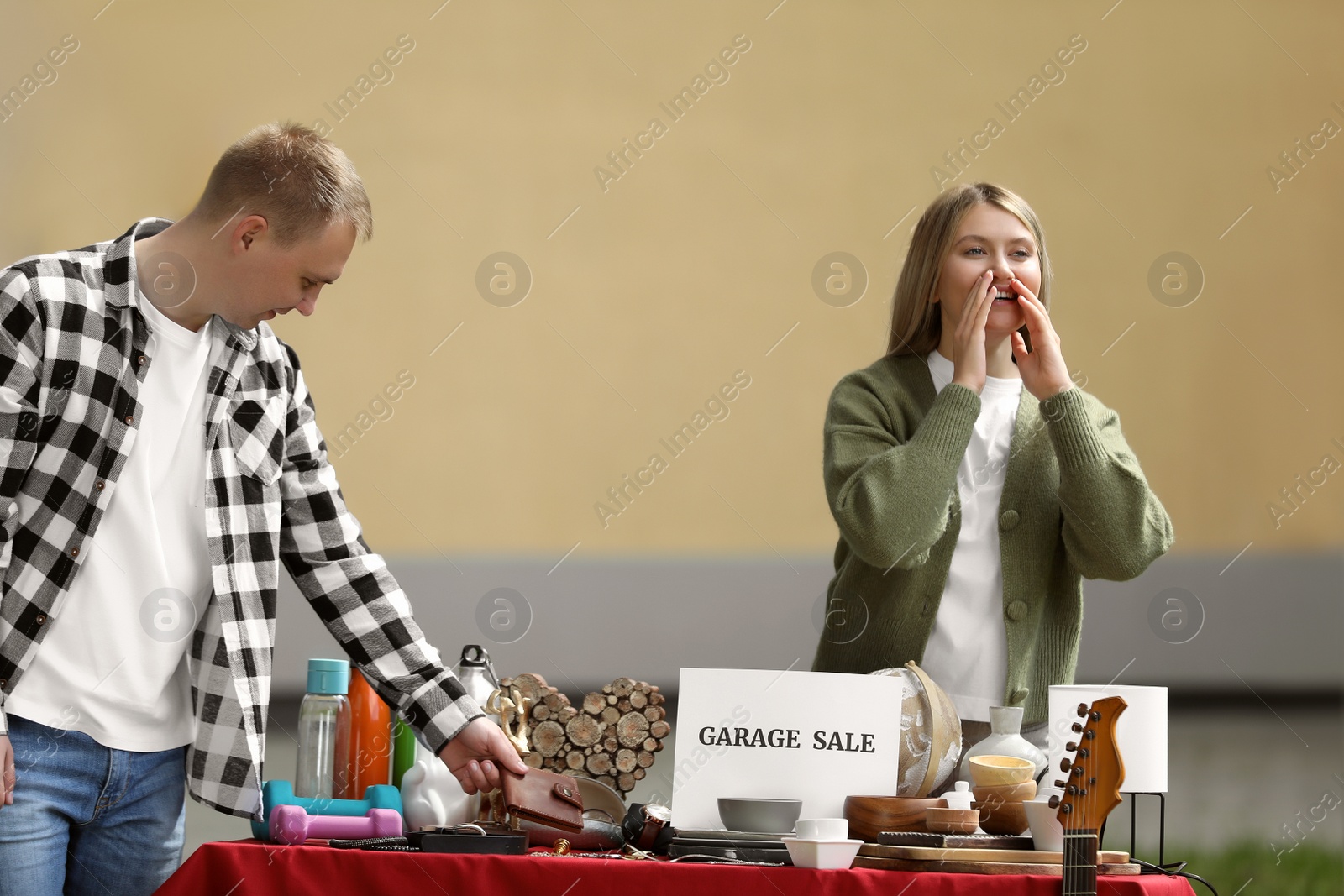 Photo of Woman inviting customers at table with different items on garage sale in yard