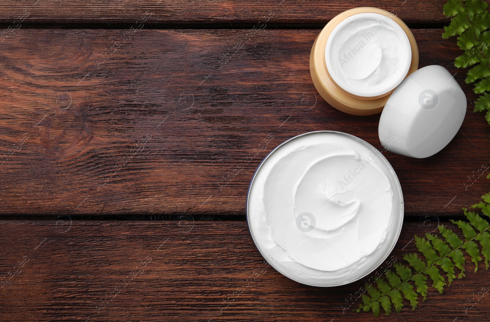 Photo of Jars of face cream and green plant on wooden table, flat lay. Space for text