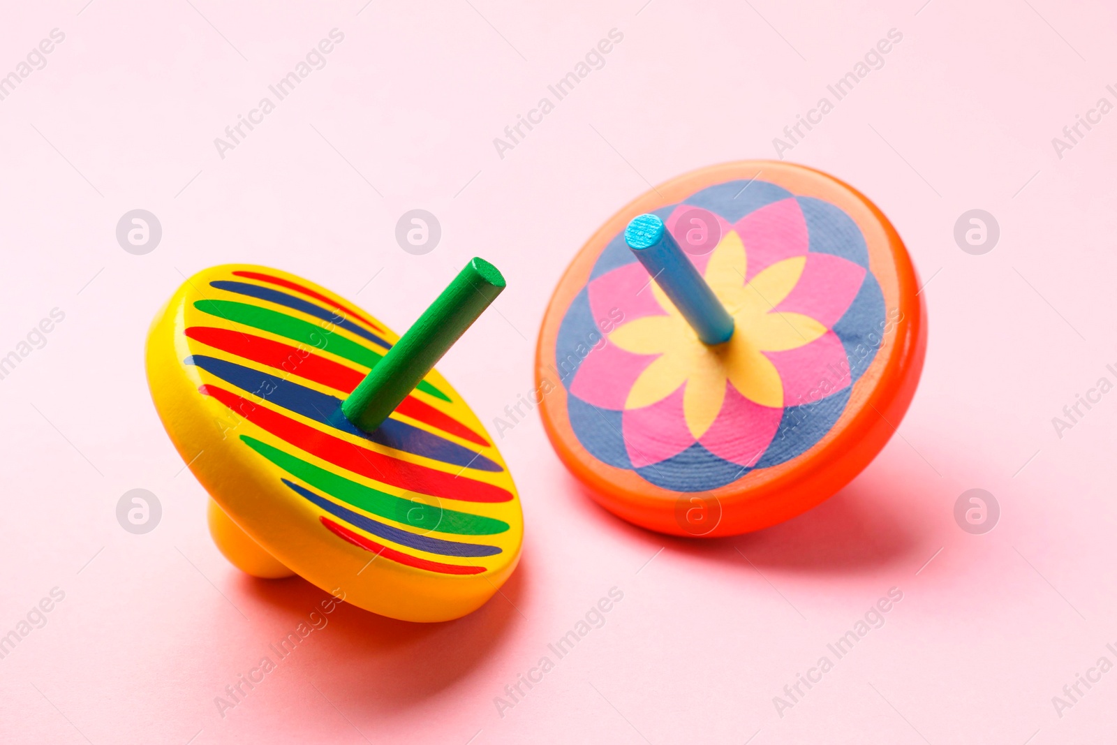 Photo of Two colorful spinning tops on pink background, closeup