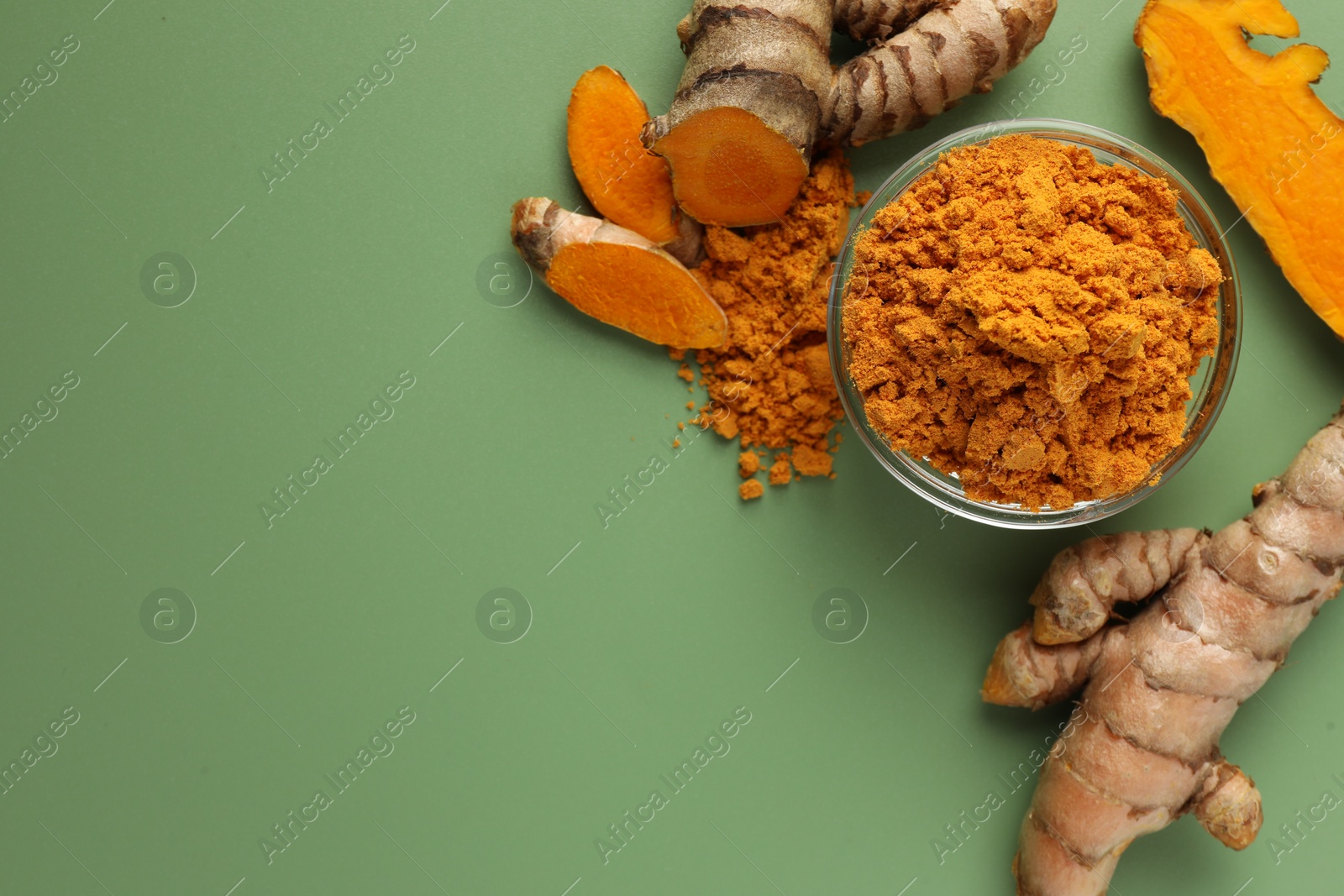 Photo of Aromatic turmeric powder and raw roots on green background, flat lay. Space for text