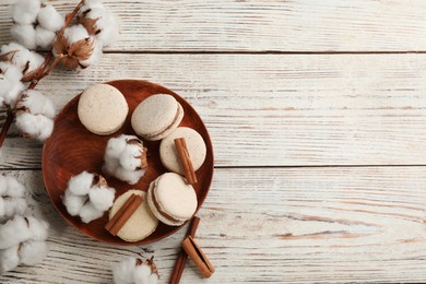 Delicious macarons and cotton flowers on white wooden table, flat lay. Space for text