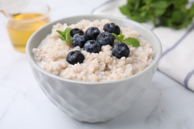 Photo of Delicious barley porridge with blueberries and mint in bowl on white marble table, closeup