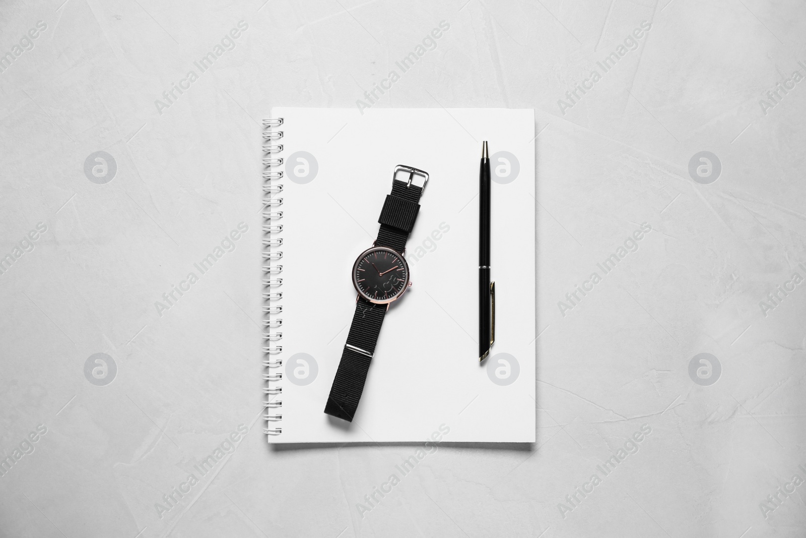 Photo of Notebook, wristwatch and pen on light grey stone table, flat lay
