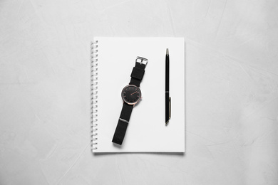 Notebook, wristwatch and pen on light grey stone table, flat lay